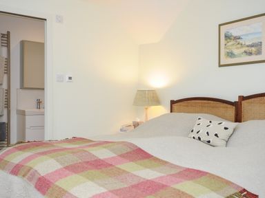 A bedroom with a double bed a checkered blanket a bedside lamp and an open bathroom door at Kirland in St Kew Highway