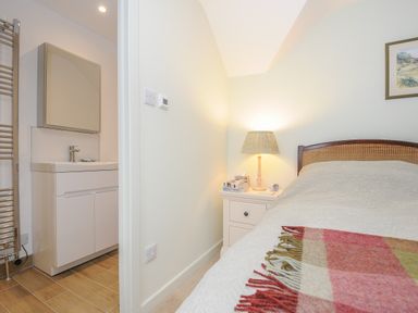 A bedroom with a bed covered by a quilt and a plaid blanket next to a nightstand with a lamp and books at Kirland in St Kew Highway