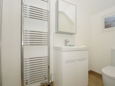 A bathroom with a white vanity unit and sink a chrome towel radiator a white toilet and a framed picture on the wall at Kirland in St Kew Highway