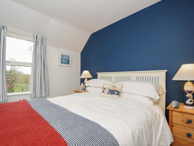 A bedroom with a bed with white bedding and blue and red blankets and wooden bedside tables with lamps at Kirland in St Kew Highway