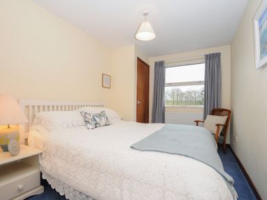 A bedroom with a bed a bedside table with a lamp and clock a wooden chair and a window at Kirland in St Kew Highway
