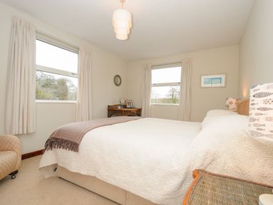 A bedroom with a bed a desk chair two windows a lamp and a framed picture at Kirland in St Kew Highway
