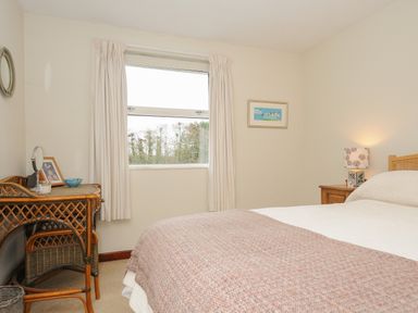 A bedroom with a bed a bedside table with a lamp a wicker desk with a chair a window and a framed picture on the wall at Kirland in St Kew Highway