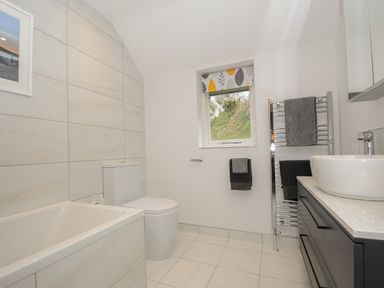 A bathroom with a bathtub toilet window with patterned blind towels on a heated towel rail and a sink with vanity unit at Kirland in St Kew Highway