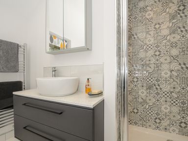 A bathroom with a sink on a countertop a mirror cabinet a towel rack and a shower with patterned tiles at Kirland in St Kew Highway