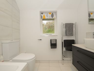 A bathroom with toilet towel rack vanity with sink and window with patterned blind at Kirland in St Kew Highway
