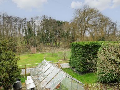 A garden with a glass greenhouse surrounded by grass shrubs trees and a wooden shed at Kirland in St Kew Highway
