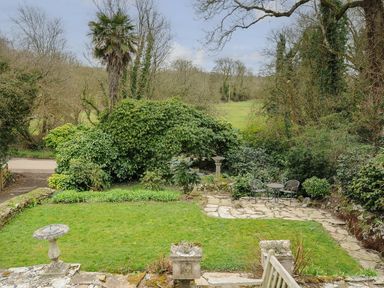 A garden with a lawn stone pathways two birdbaths a table with two chairs and surrounding trees and bushes at Kirland in St Kew Highway