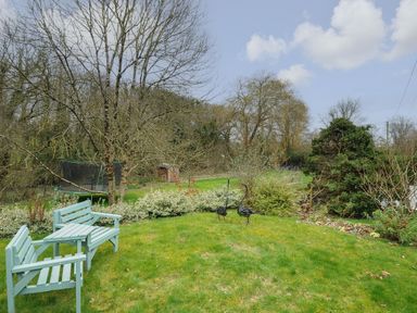 A garden with two blue wooden benches on grass and trees in the background at Kirland in St Kew Highway
