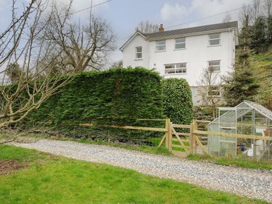 A white two-story house with large bushes a wooden gate and a greenhouse on a gravel path at Kirland in St Kew Highway