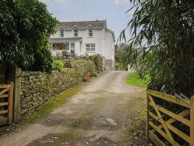 A driveway leading to a white two-story house with stone walls and wooden gates at Kirland in St Kew Highway