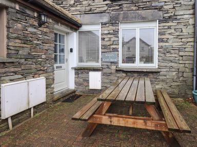 A wooden picnic table on a brick patio outside a stone building with two windows and a door at Jennys 2 Croft Barn in Hawkshead