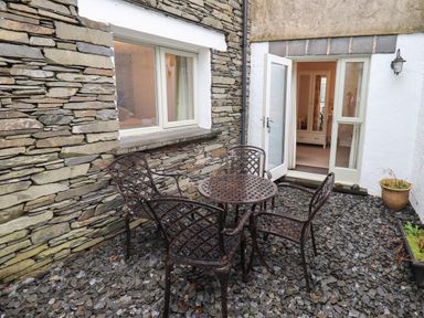 A stone patio with metal table and four chairs outside a house with open glass door at Jennys in Hawkshead