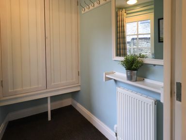 A small hallway with a radiator under a shelf holding a potted plant and a window with curtains at Jennys in Hawkshead