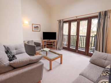A living room with sofas a glass coffee table a TV and glass doors leading to a balcony at Beechside in Ambleside