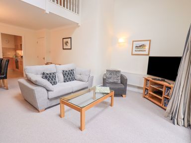 A living room with a sofa and armchair a glass coffee table and a TV on a wooden stand at Beechside Ambleside