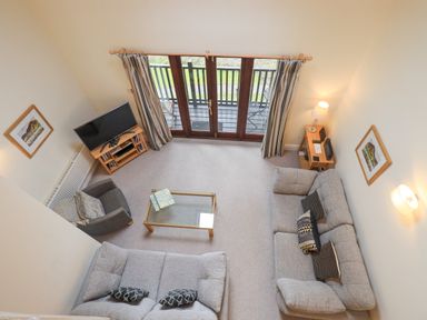 A living room with two sofas an armchair a glass coffee table a television and doors leading to a balcony at Beechside in Ambleside