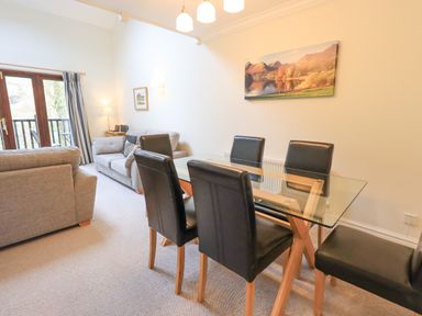 A dining area with glass table and black chairs next to a living room with grey sofas at Beechside in Ambleside