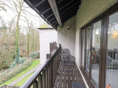 A balcony with two metal chairs and a round table overlooking a garden at Beechside in Ambleside