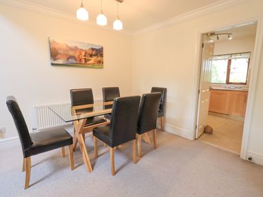 A dining room with a glass table and six black chairs and a painting on the wall at Beechside Ambleside