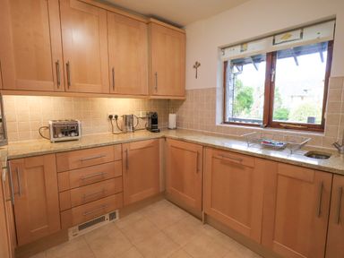A kitchen with wooden cabinets a countertop with toaster kettle coffee machine and a window with a dish drying rack at Beechside in Ambleside