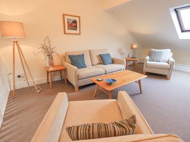 A living room with beige sofas, wooden coffee table, side tables with lamps, and a skylight window at Beechside Ambleside