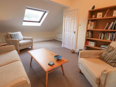 A living room with beige sofa and armchairs a wooden coffee table and a bookshelf at Beechside in Ambleside