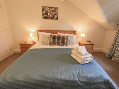 A bedroom with a bed with blue quilt and folded towels on top two wooden nightstands with lamps and a painting above the bed at Beechside in Ambleside