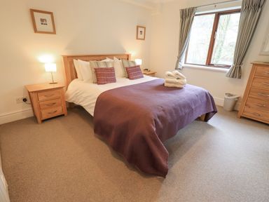 A bedroom with a double bed with pillows and folded towels bedside tables and a window with curtains at Beechside in Ambleside