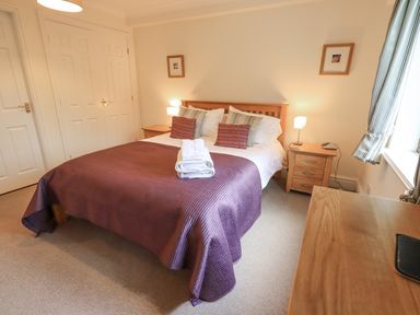 A bedroom with a double bed with pillows and folded towels bedside tables with lamps and curtains at Beechside in Ambleside
