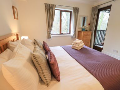 A bedroom with a bed with pillows and folded towels a window with curtains and a wooden dresser at Beechside in Ambleside