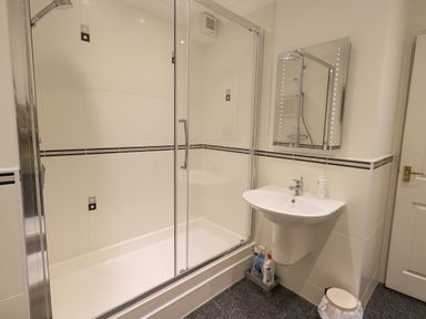 A bathroom with a shower enclosure sink mirror and cleaning supplies at Beechside in Ambleside