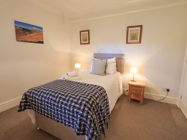 A bedroom with a single bed a side table with lamps on each side and framed pictures on the walls at Beechside in Ambleside