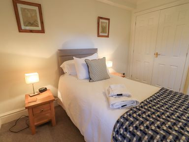 A bedroom with a single bed pillows and folded towels bedside tables with lamps and framed pictures on the wall at Beechside in Ambleside