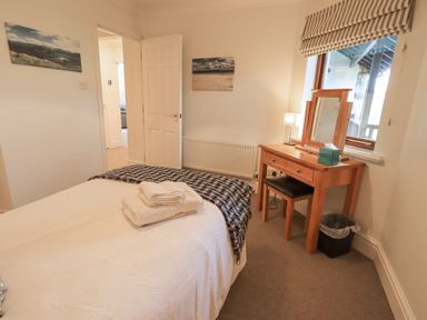 A bedroom with a bed, folded towels, a wooden dressing table with a mirror and lamp at Beechside in Ambleside