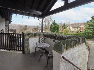 A covered patio area with a metal table and two chairs surrounded by stone walls at Beechside in Ambleside