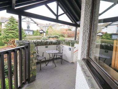 A covered outdoor patio with a small metal table and two chairs overlooking residential houses at Beechside in Ambleside
