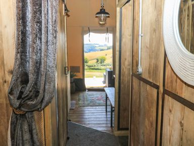 A wooden hallway with a curtain on the left and a round mirror on the right at Semira Tent Lodge in Blackawton