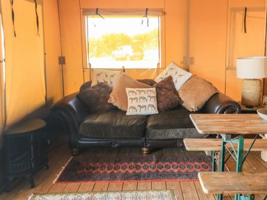 A tent interior with a leather sofa and cushions a wooden table with benches a lamp and a heater at Semira Tent Lodge in Blackawton