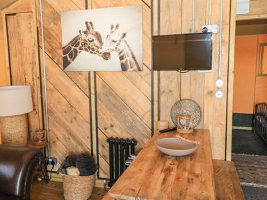 A wooden wall with a mounted TV and a photograph of two giraffes above a wooden table with decorative items at Semira Tent Lodge in Blackawton
