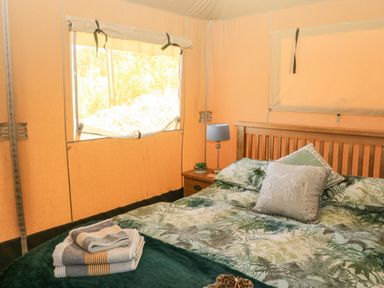 A bedroom with a bed with patterned bedding and pillows a bedside table with a lamp and folded towels on the bed at Semira Tent Lodge in Blackawton
