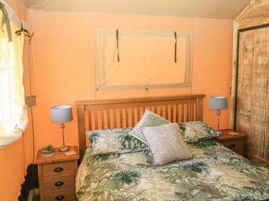A bedroom with a wooden bed with patterned bedding and two bedside tables with lamps at Semira Tent Lodge Blackawton