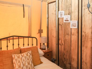 A bedroom corner with a metal bed frame pillows bedside table with a lamp and wooden panel walls with animal pictures at Semira Tent Lodge in Blackawton