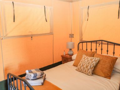 A bed with pillows and folded towels next to a nightstand with a lamp inside a tent at Semira Tent Lodge in Blackawton