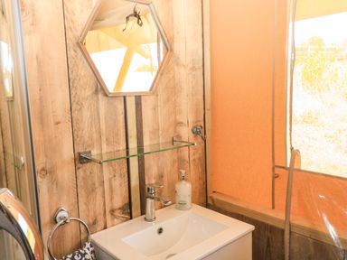 A bathroom sink with a faucet towel ring soap dispenser and a hexagonal mirror at Semira Tent Lodge in Blackawton