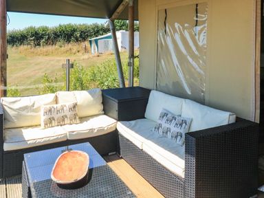 An outdoor seating area with two wicker sofas with white cushions and elephant print pillows at Semira Tent Lodge in Blackawton