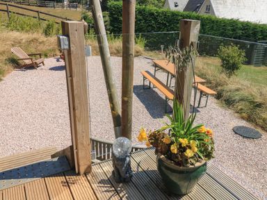 A wooden deck with a large green plant pot and a small elephant statue a wooden picnic table with benches on a gravel area and a wooden chair in a garden at Semira Tent Lodge in Blackawton