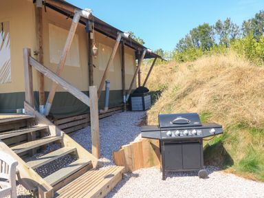 An outdoor area with stairs leading to a tent structure and a barbecue grill on gravel at Semira Tent Lodge in Blackawton
