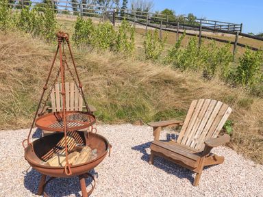 An outdoor seating area with wooden Adirondack chairs and a metal fire pit on gravel at Semira Tent Lodge in Blackawton