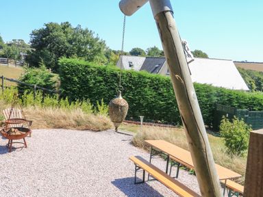 An outdoor patio with a hanging lantern a fire pit bench seating and bushes at Semira Tent Lodge in Blackawton